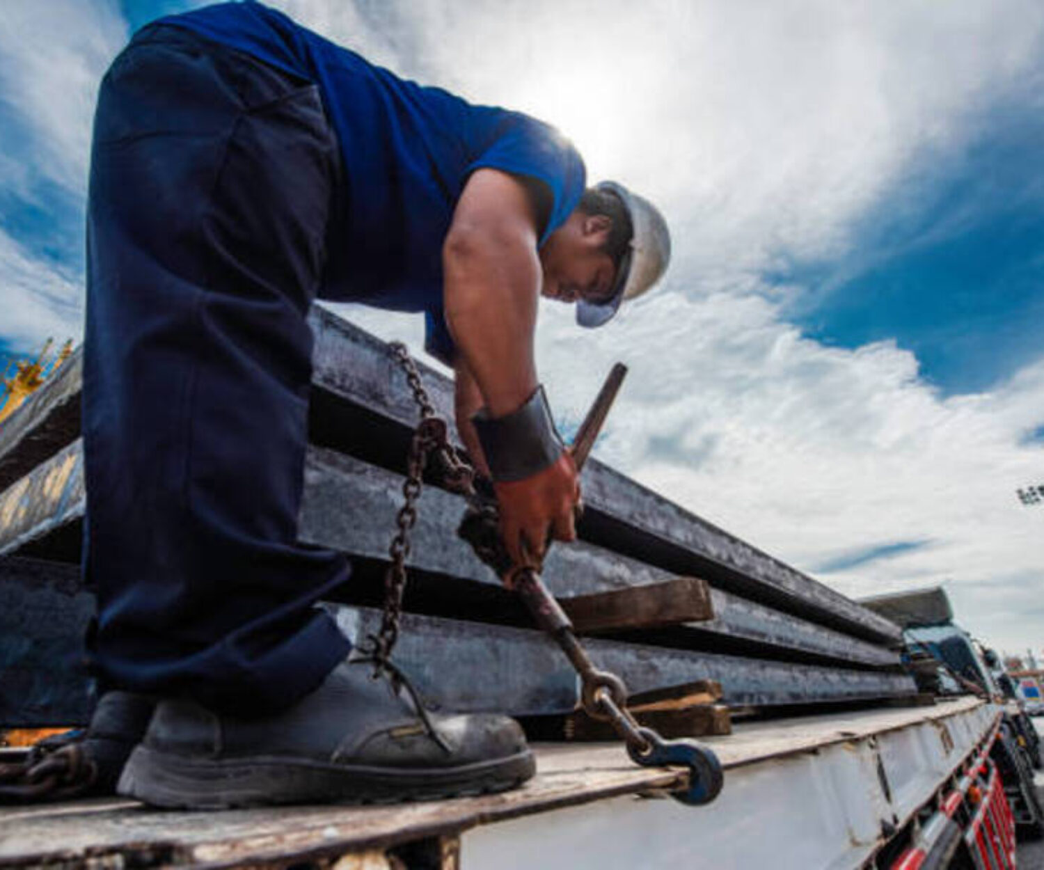 Driver foreman in takes lashing securing pressure strength fastening of the lashing chains to secured the cargo shipment fo the steel slabs carry on the truck trailer before shifting or move travel transports to cargo to destination