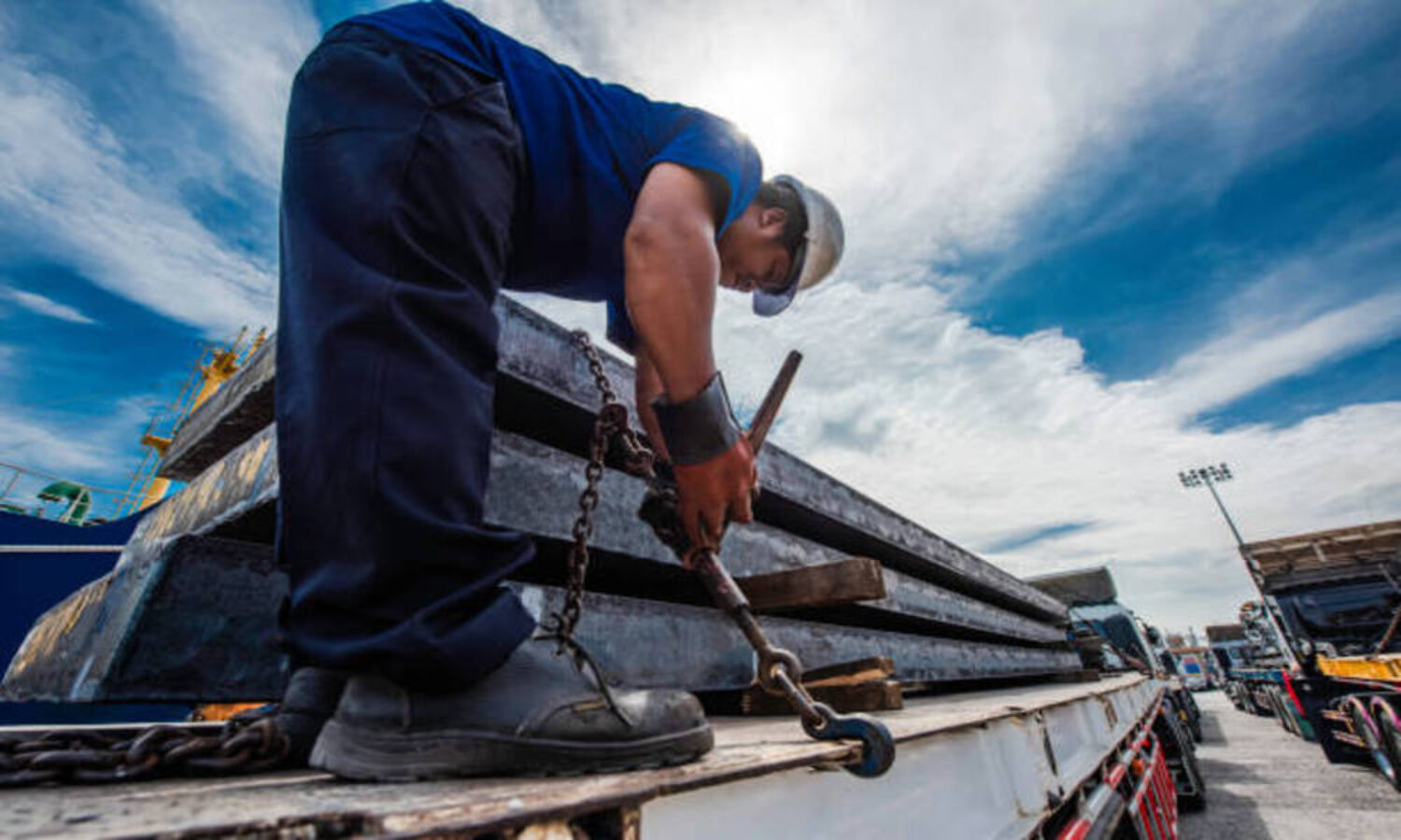 Driver foreman in takes lashing securing pressure strength fastening of the lashing chains to secured the cargo shipment fo the steel slabs carry on the truck trailer before shifting or move travel transports to cargo to destination